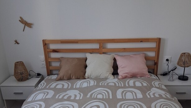Een slaapkamer met een bed, houten hoofdbord, nachtkastjes, lampen en wanddecoraties.