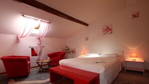 Ein Schlafzimmer mit einem Bett, zwei roten Stühlen, einem kleinen Tisch, einer Nachttischlampe und einem Fenster mit Vorhängen.