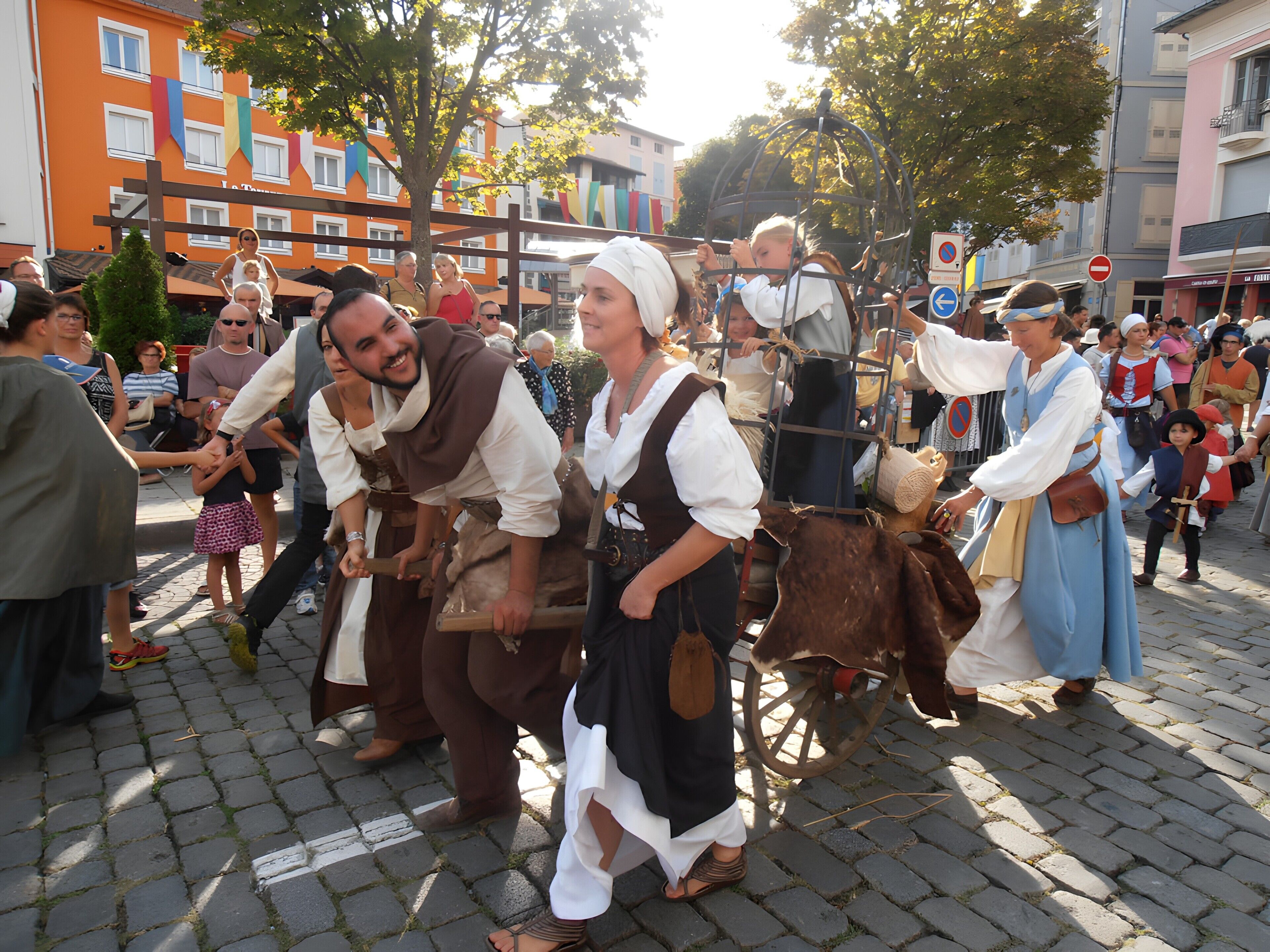 A historical reenactment with participants in period costumes, a crowd of spectators, and a cobblestone street.