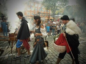 A cobblestone street with people in historical costumes, a building with a sign reading 'La Taverne,' and a person carrying a basket.