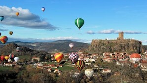 A town with a prominent tower on a hill, surrounded by colorful hot air balloons. - Guest Room 'Chambre Rivage' with Shared Terrace & Garden, Wi-Fi (Polignac)