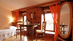 A wooden room with a bed, a table, chairs, a mirror, and a window with curtains. - “Romance” Guest Room with Shared Terrace, Garden, and Wi-Fi (Polignac)