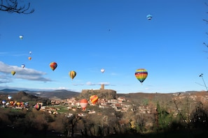 A town with a castle on a hill, surrounded by a valley and hot air balloons in the sky. - Guest Room “Chambre Rêverie” with Shared Terrace, Garden and Wi-Fi (Polignac)
