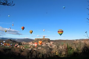 Een stad met een kasteel op een heuvel, omringd door een vallei en luchtballonnen aan de lucht.