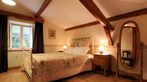 A bedroom with a bed, bedside lamps, a wooden-framed mirror, and a window with curtains.