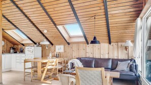 Um interior de madeira aconchegante, com uma área de jantar, um sofá e uma cozinha ao fundo.