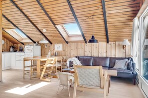 A cozy wooden interior with a dining area, a sofa, and a kitchen in the background. - Lovely holiday home with wood-burning stove, close to the North Sea in. (Thisted)