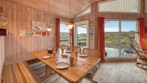 Un interno in legno con un tavolo da pranzo, sedie e una vista attraverso ampie finestre.