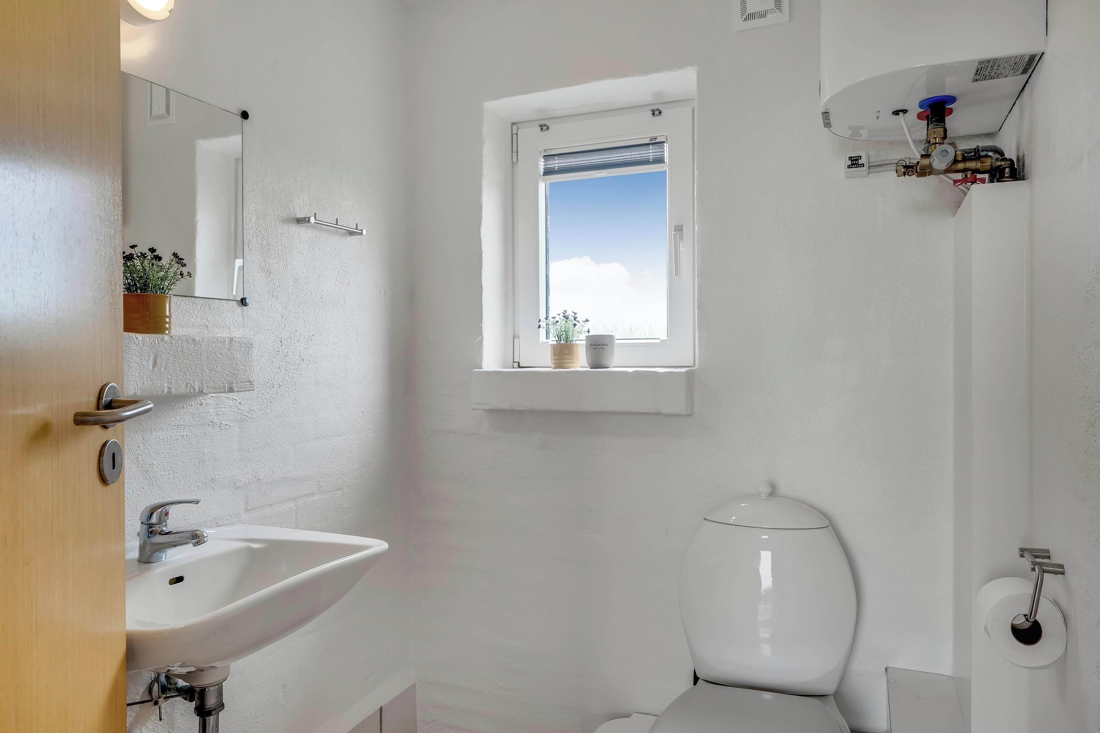 Un baño con lavamanos blanco, inodoro y ventana con vistas al cielo.