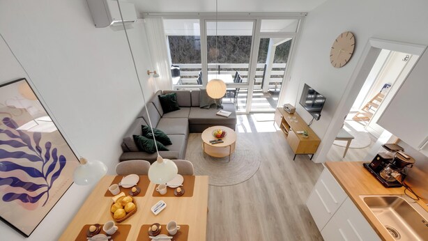 Eine moderne Küche mit Essbereich, ein Wohnzimmer mit Sofa und ein Balkon mit Blick.