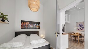Ein modernes Schlafzimmer mit Bett, Stadtbildgemälde, Pendelleuchte und einem Essbereich mit Tisch und Stühlen.