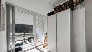 Ein Zimmer mit einer Schiebetür und einem Balkon, einem weißen Kleiderschrank und einem kleinen Holzstuhl.