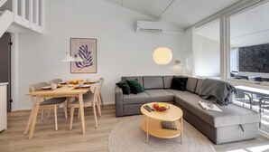 Ein modernes Wohnzimmer mit Essbereich, einem grauen Sofa, einem runden Couchtisch und einer Treppe.
