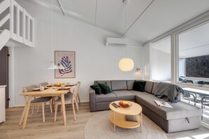 Una sala de estar moderna con comedor, un sofá gris, una mesa redonda de centro y una escalera.