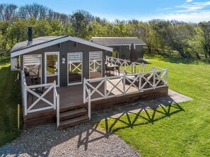 Une cabane dotée d’une terrasse, d’un espace extérieur couvert avec des sièges, et d’un numéro « 2 » sur la porte.