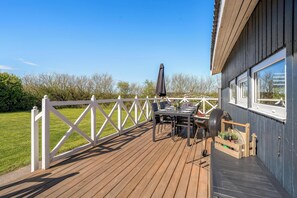 Une terrasse avec une table et des chaises, un barbecue et une clôture blanche.