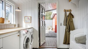 Een wasruimte met een wasmachine, een houten aanrechtblad, een kapstok en een bed met een kussen.