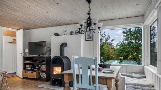 Ein gemütliches Zimmer mit Holzbalkendecke, Kamin, Fernseher und einem Fenster mit Blick ins Grüne.