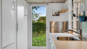 Eine moderne Küche mit Spüle aus Edelstahl, einer Tür zu einem Garten und einem kleinen Fenster.