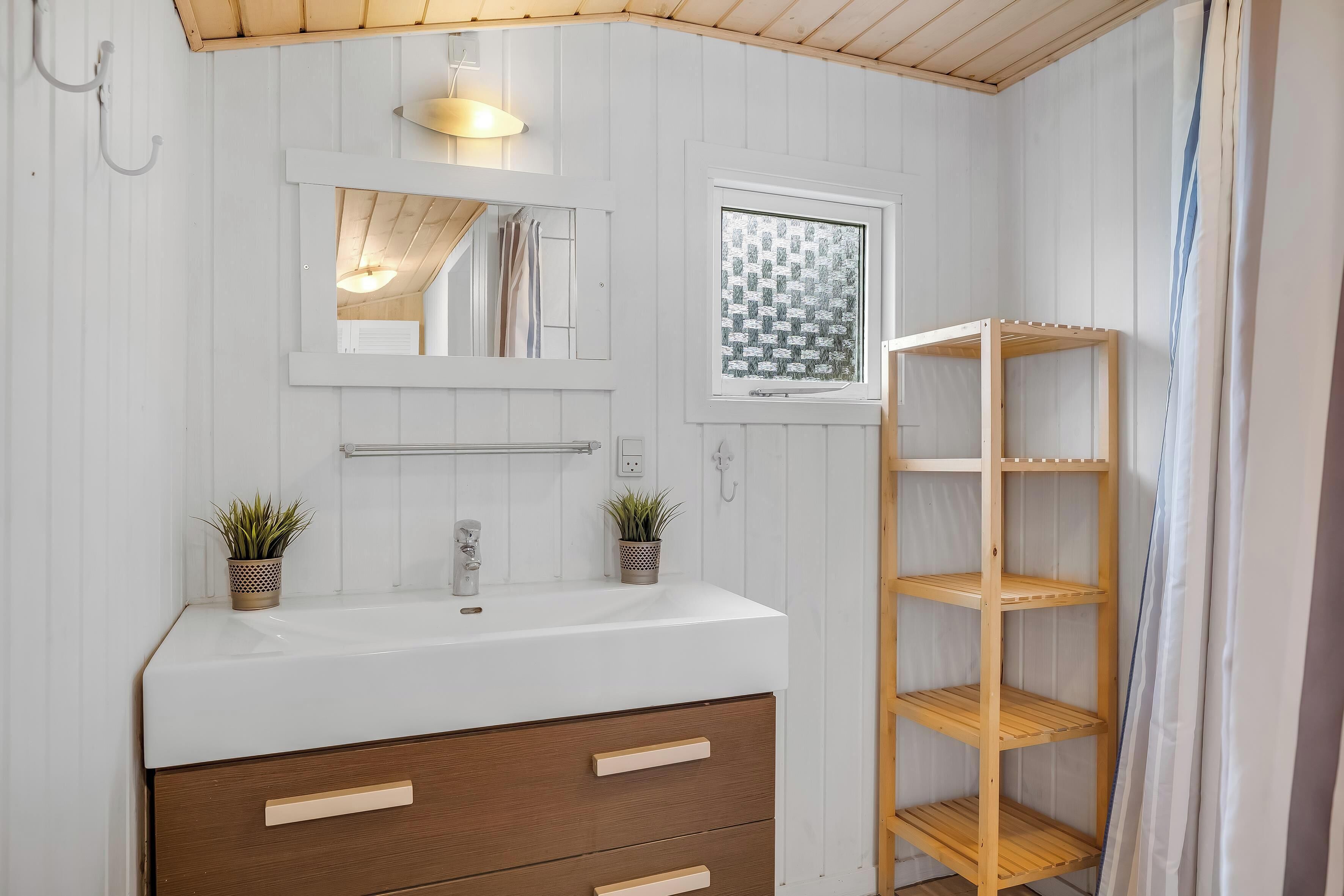 Une salle de bain avec un meuble-lavabo blanc, des étagères en bois, un miroir et deux plantes en pot.