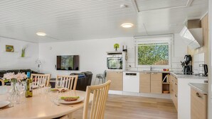 Een moderne keuken met witte kasten, een eethoek met een ronde tafel en stoelen, en een aan de muur bevestigde televisie.