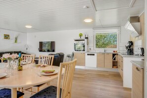 A modern kitchen with white cabinetry, a dining area with a round table and chairs, and a TV mounted on the wall. - Family-friendly holiday home with large wilderness bath, close to the water. (Vestervig)