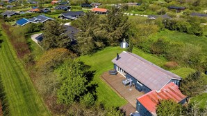 Luchtbeeld van een woonwijk met huizen, een groot open gazon en een waterpartij op de achtergrond.