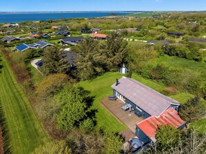 An aerial view of a residential area with houses, a large open lawn, and a body of water in the background. - Family-friendly holiday home with large wilderness bath, close to the water. (Vestervig)
