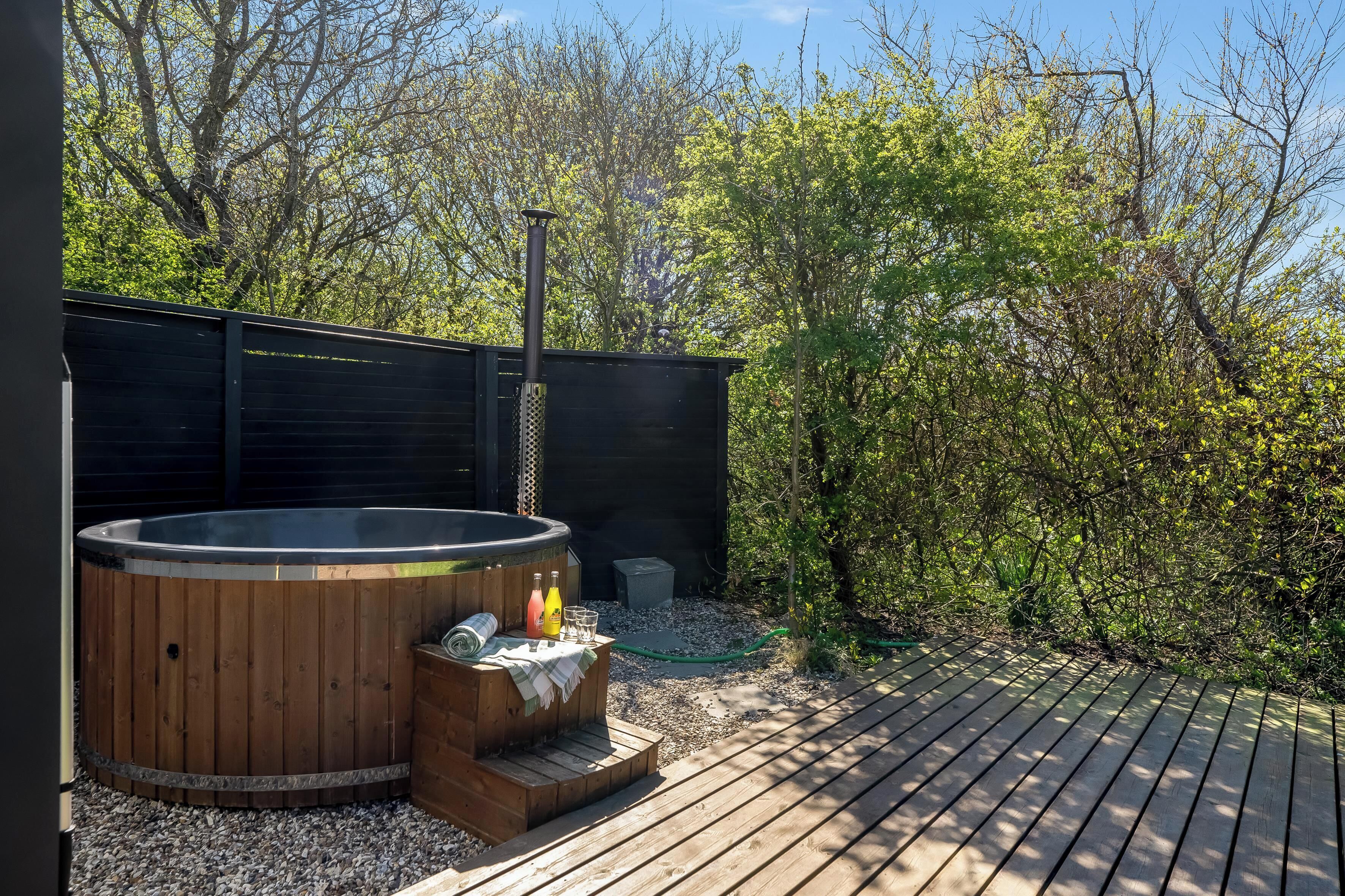 A hot tub with a wooden exterior, a wooden deck, and a fenced garden area.
