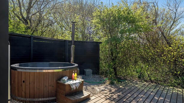Een hottub met een houten buitenkant, een houten terras en een omheinde tuin.