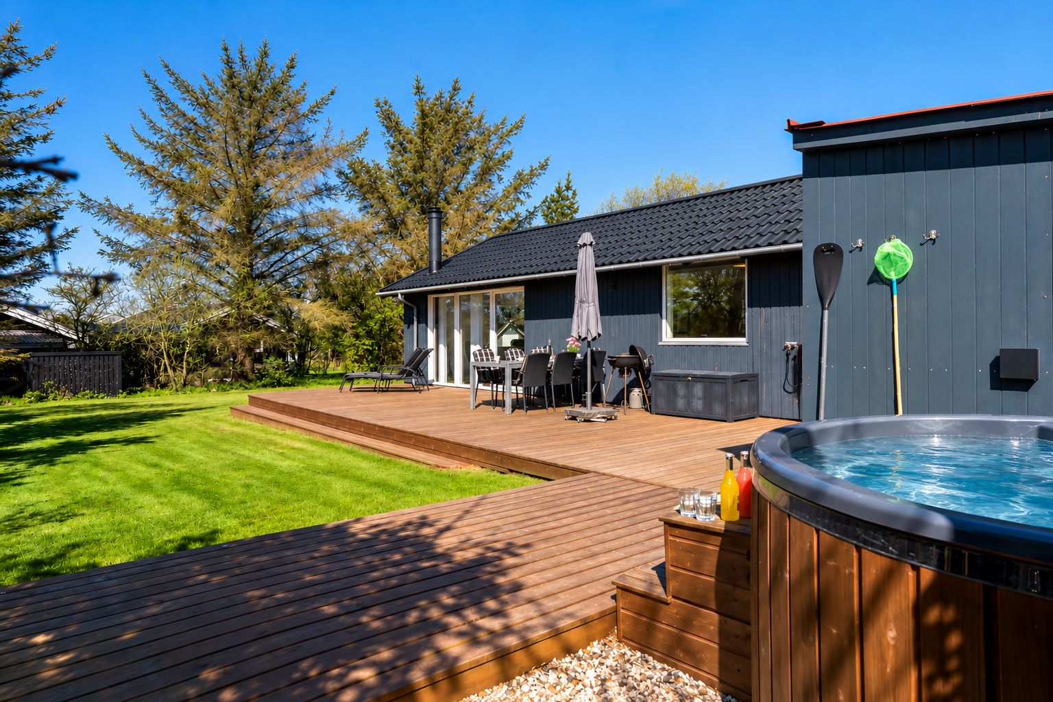 Una terraza moderna al aire libre con un jacuzzi, una zona de barbacoa y un conjunto de asientos.
