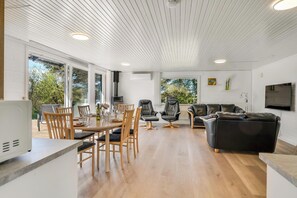 A spacious living area with a dining table, chairs, a sofa, and a TV mounted on the wall. - Family-friendly holiday home with large wilderness bath, close to the water. (Vestervig)
