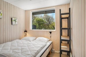 Ein Schlafzimmer mit Bett, Fenster, einer Leiter und einem an der Wand befestigten Regal.