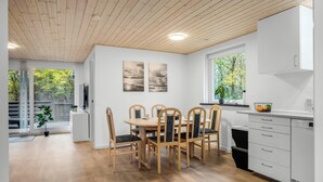 A modern kitchen with wooden cabinets, a dining table with chairs, and a large window with a view of greenery. - Cozy holiday home with a wilderness bath and covered terrace. (Hurup Thy)