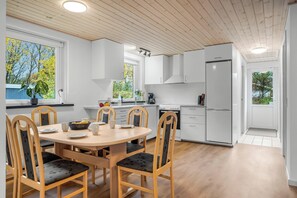 Una cocina moderna con armarios blancos, una mesa de comedor con sillas y vistas a árboles por la ventana.