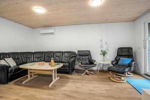 Una sala de estar moderna con un sofá de cuero negro, una mesa redonda de centro, un sillón de cuero negro y una mesita auxiliar con una planta.