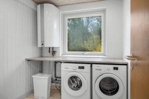 A laundry room with two washing machines, a window with a view of trees, and a white radiator.