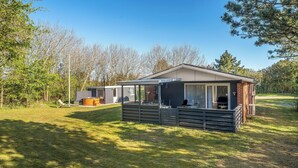 A single-story cabin with a deck, a covered outdoor seating area, and a large window. - Cozy holiday home with a wilderness bath and covered terrace. (Hurup Thy)