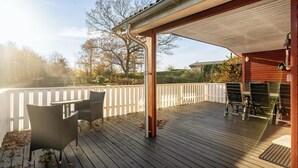 Une terrasse en bois avec des meubles d’extérieur, une clôture blanche et des arbres en arrière-plan.