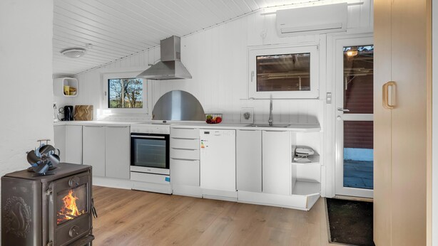 Une cuisine moderne avec des meubles blancs, un poêle à bois, un four encastré et une fenêtre donnant sur une terrasse.