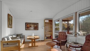 Une pièce comprenant un canapé en bois, des fauteuils en cuir, une table en bois, une bibliothèque et une grande fenêtre.
