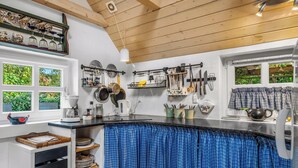 Een keuken met een houten plafond, een zwart aanrecht en een raam met uitzicht op groen.