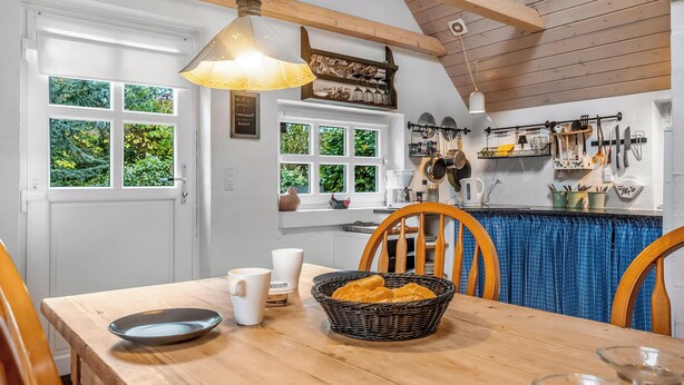 Een keuken met houten balken, witte kasten en een blauw geruit tafelkleed.