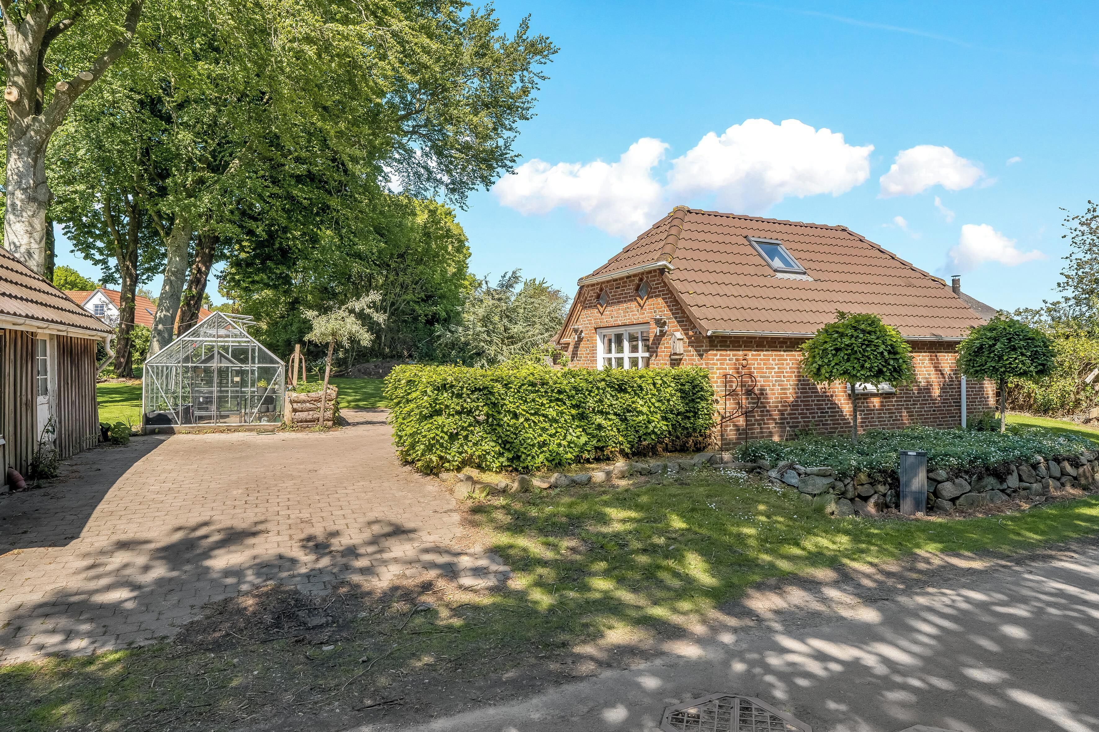 A brick house with a tiled roof, a greenhouse, and a stone wall with plants.