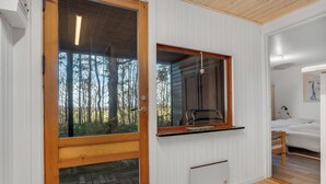 Una stanza con una porta in legno, una finestra che dà su degli alberi, un letto con biancheria bianca e un muro bianco con un quadro.