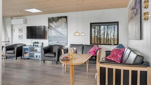 Un soggiorno moderno con soffitto in legno, una televisione a schermo piatto, un tavolo da pranzo e un divano con cuscini.