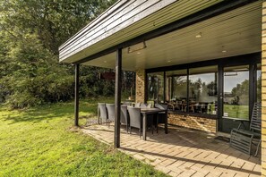 Un espace extérieur abrité, doté de tables et de chaises, entouré d’un mur de briques et de portes vitrées.