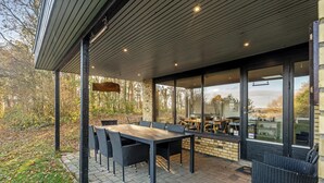 Una terrazza esterna con tavolo e sedie, un lampadario sospeso e vista sugli alberi circostanti.