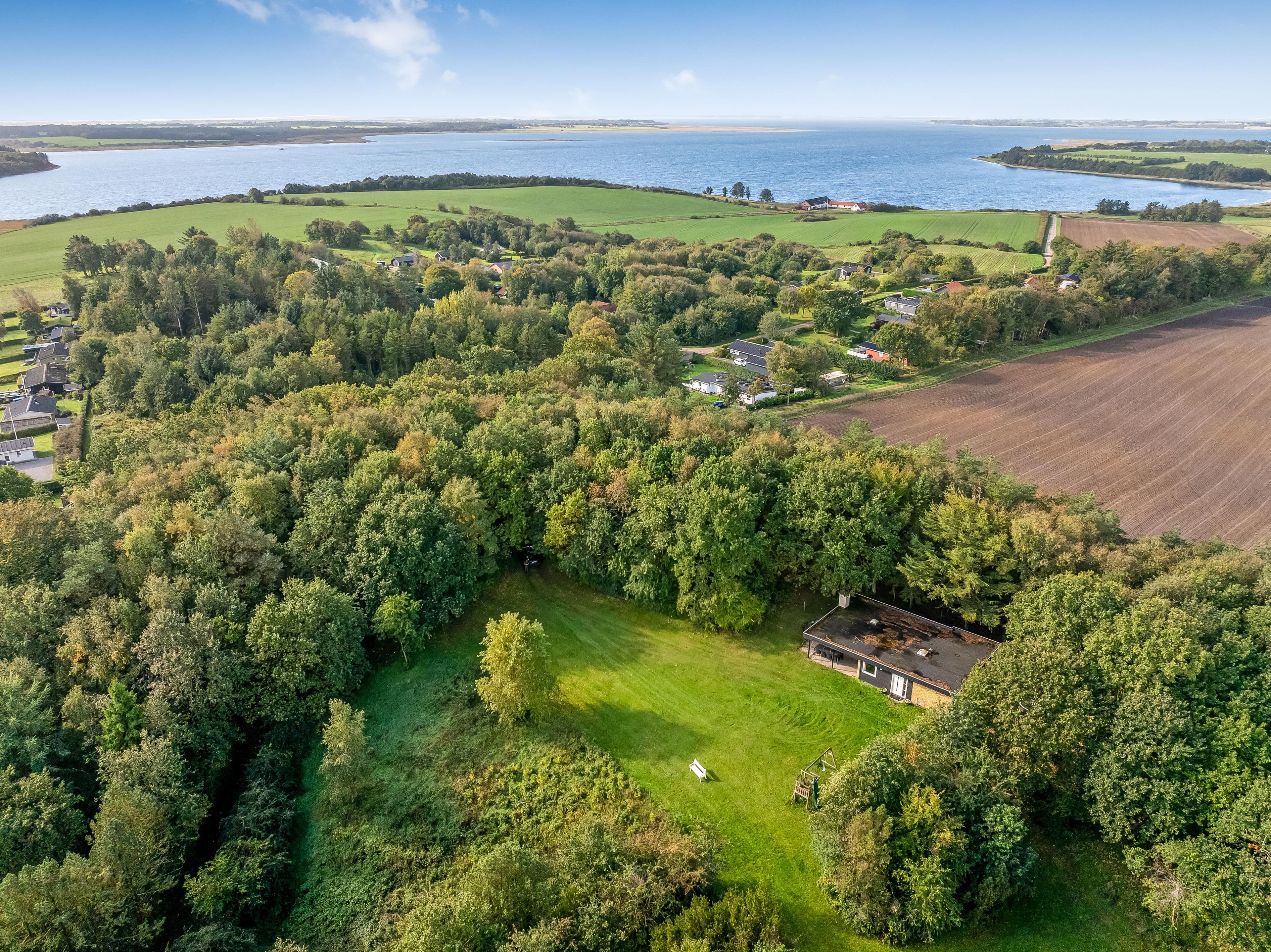 An aerial view of a rural property with a large field, a small house, and a body of water in the background.
