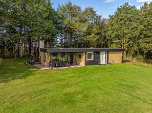 A modern house with a patio, surrounded by a grassy yard and trees. - Lovely holiday home with wilderness bath and a view of the fjord. (Roslev)
